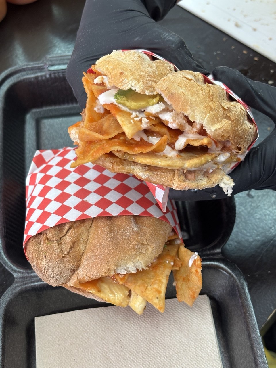 A torta opened on red-and-white checkered paper: potato chips, crema, cheese, jalapeño, tomato.