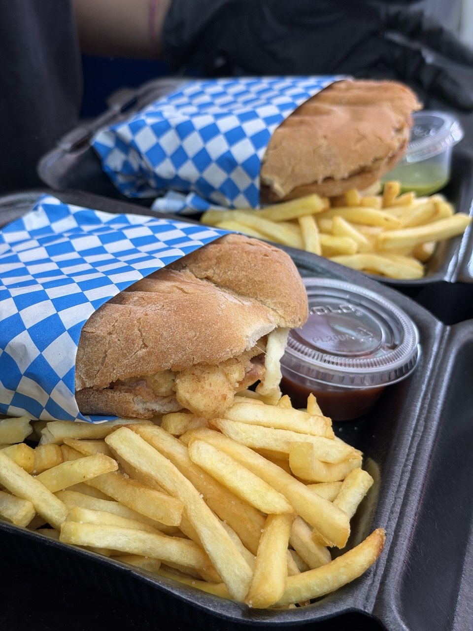 Two tortas on blue-and-white checkered paper on a black tray, with french fries and two salsas.